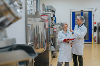 Julie en Thijs van JUGE in de productieomgeving met clipboard en haarnetjes